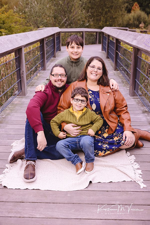 Family of 4 poses smiling while sitting on a blanket during their early fall family photos