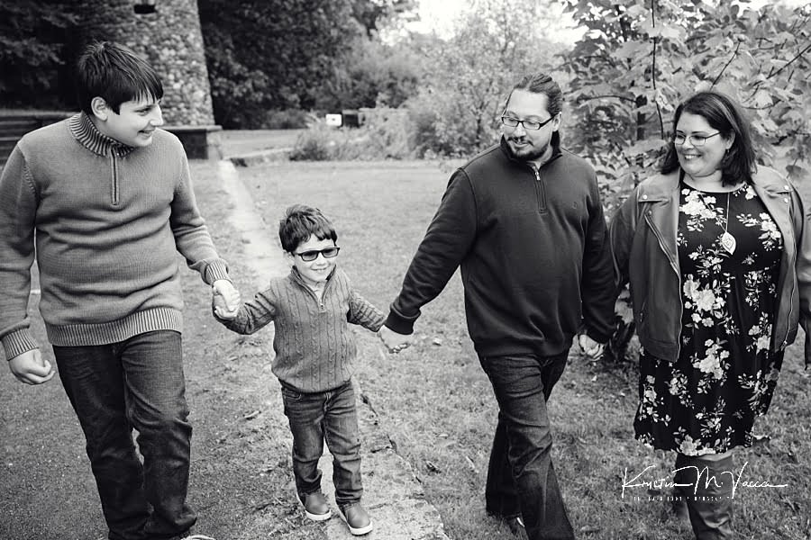 Black and white photo of family of 4 walking holding hands during their early fall family photos