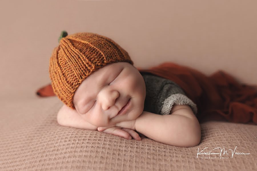 Sleeping newborn boy smiles wearing a pumpkin hat during his photoshoot