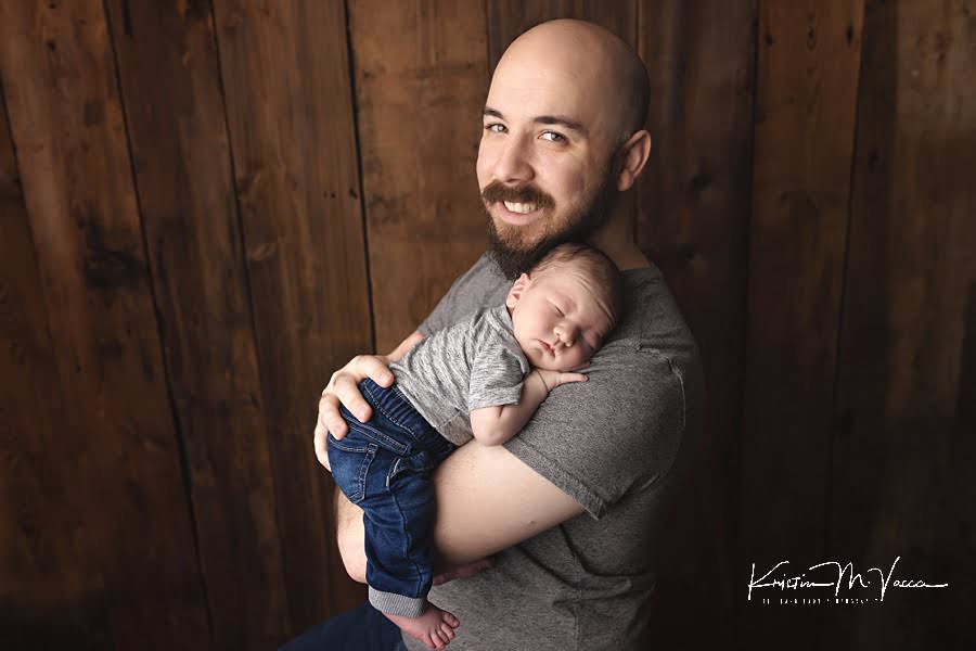 Dad holds his baby boy sleeping on his arm during their fall studio newborn photos