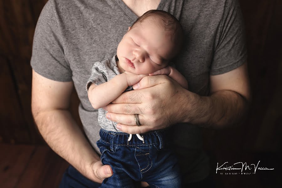 Closeup of sleeping newborn in his Dad's arms during their photoshoot