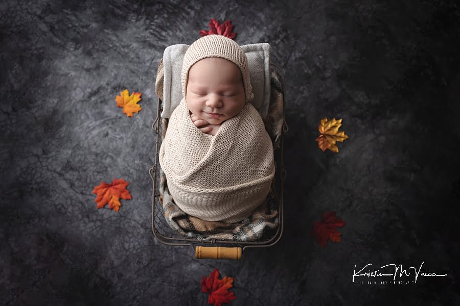 Sleeping baby boy wrapped in cream and leaves around during his fall studio newborn photos