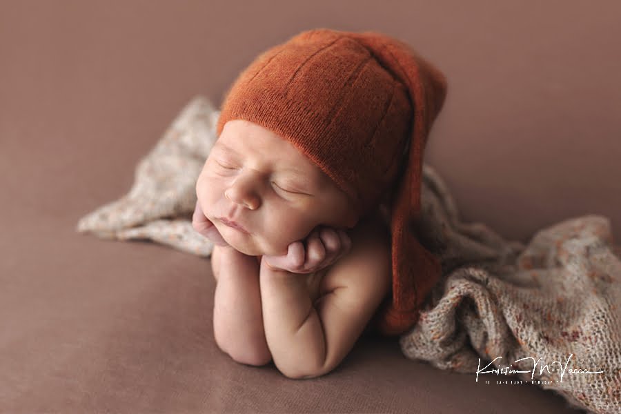 Side view of froggie pose in an orange hat during his fall woodland newborn photos
