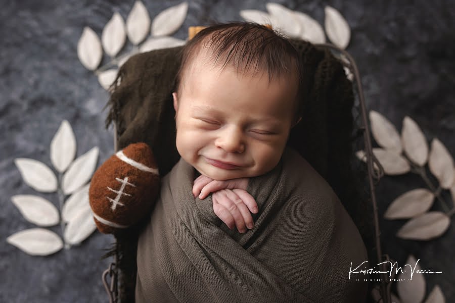 Closeup of smiling sleeping baby boy with a football during his fall woodland newborn photos
