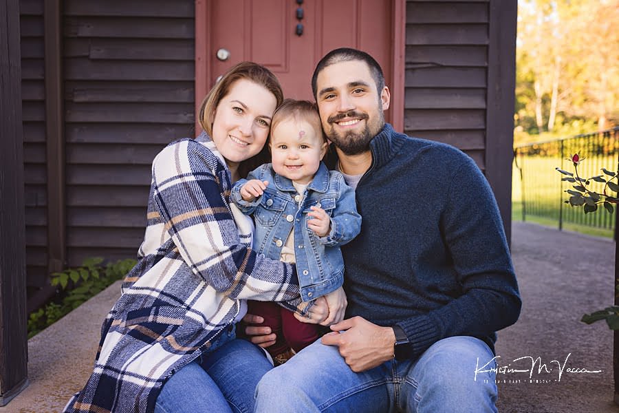 Mom & Dad with their baby girl snuggle on a front step during their family fall photoshoot