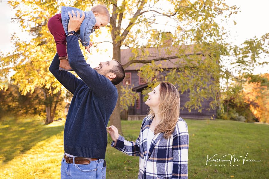 Dad tosses his baby girl in the air while Mom watches during their family fall photoshoot