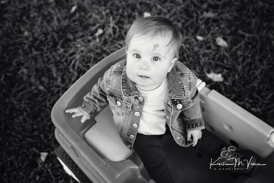 Black and white photos of one year old girl sitting in her wagon looking up during her photoshoot
