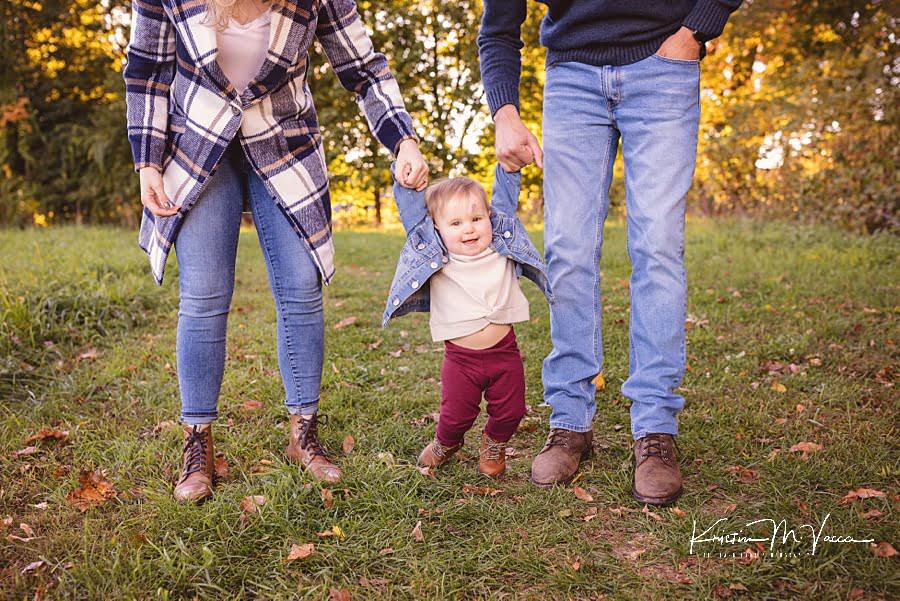 Closeup of Mom & Dad holding baby girl's hands while she walks during their photoshoot