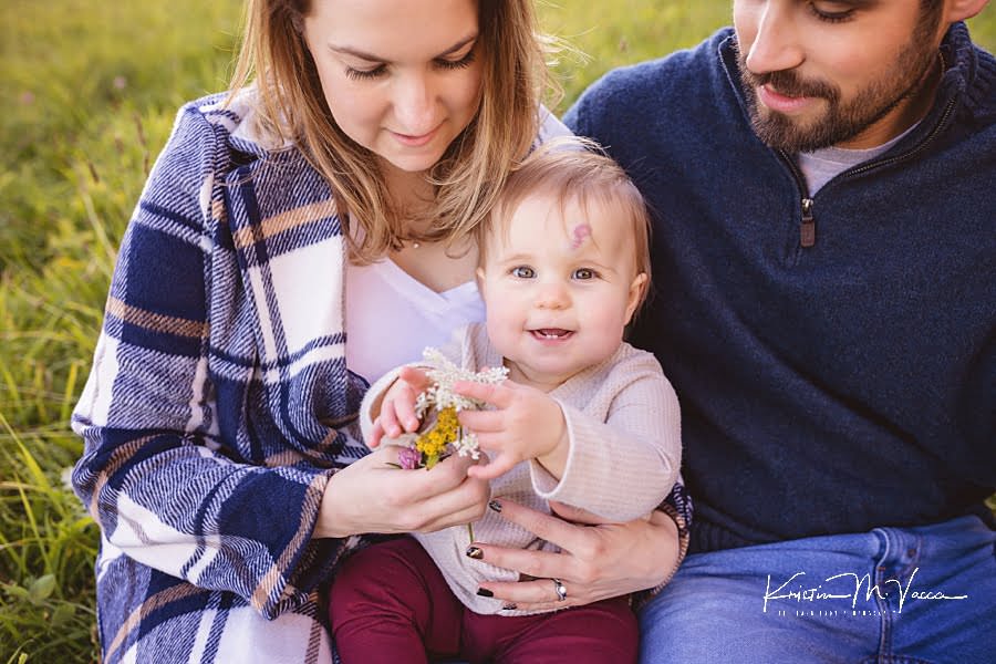 Close up of baby girl reaching at a dandelion flower and smiling during their family fall photoshoot