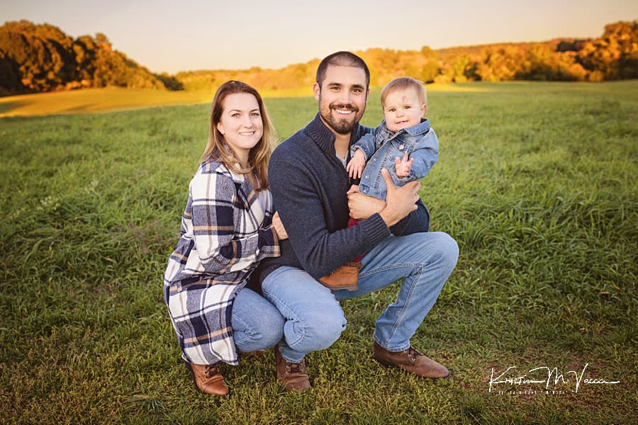 Mom & Dad squat down on the grass with their baby girl during their family fall photoshoot