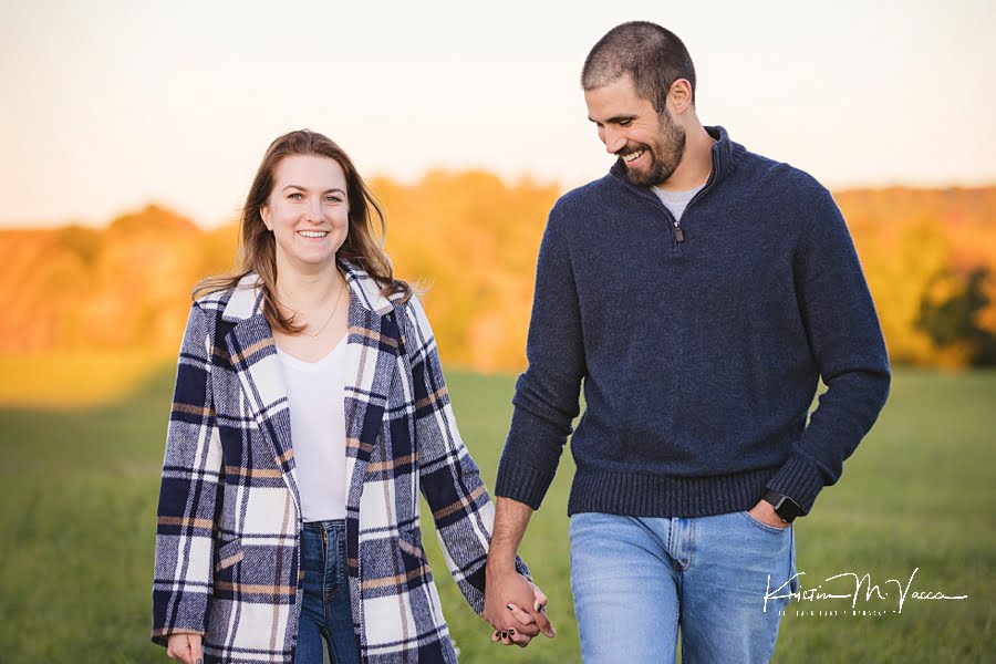 A young male and female couple holds hands walking and laughing during their photoshoot