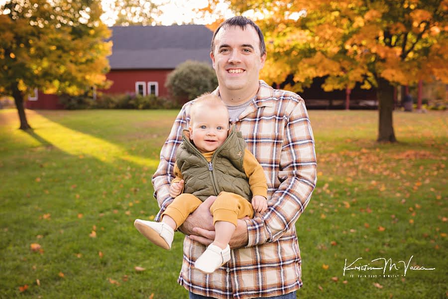 Dad holding his smiling baby boy during their happy fall family photos