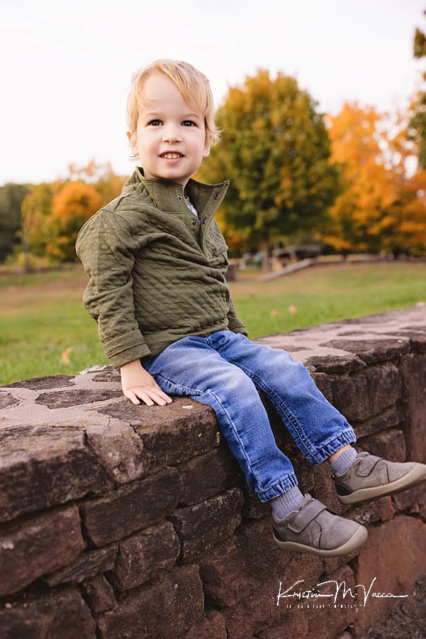 Young boy sits on a rock wall smiling during his family photoshoot