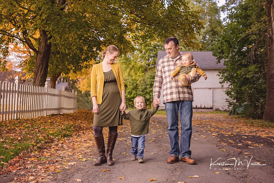 Mom, Dad, and baby brother look down at their smiling first child walking during their family photoshoot