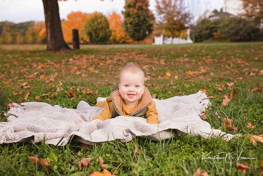 Baby boy lies on his stomach on a blanket smiling during his happy fall family photos