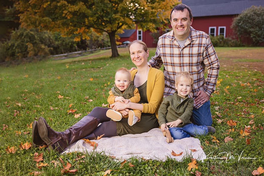 Family of 4 sits on a blanket smiling during their happy fall family photos
