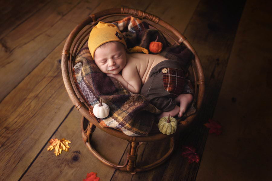 Sleeping newborn baby boy smiles lying in a fall themed scene during his photoshoot