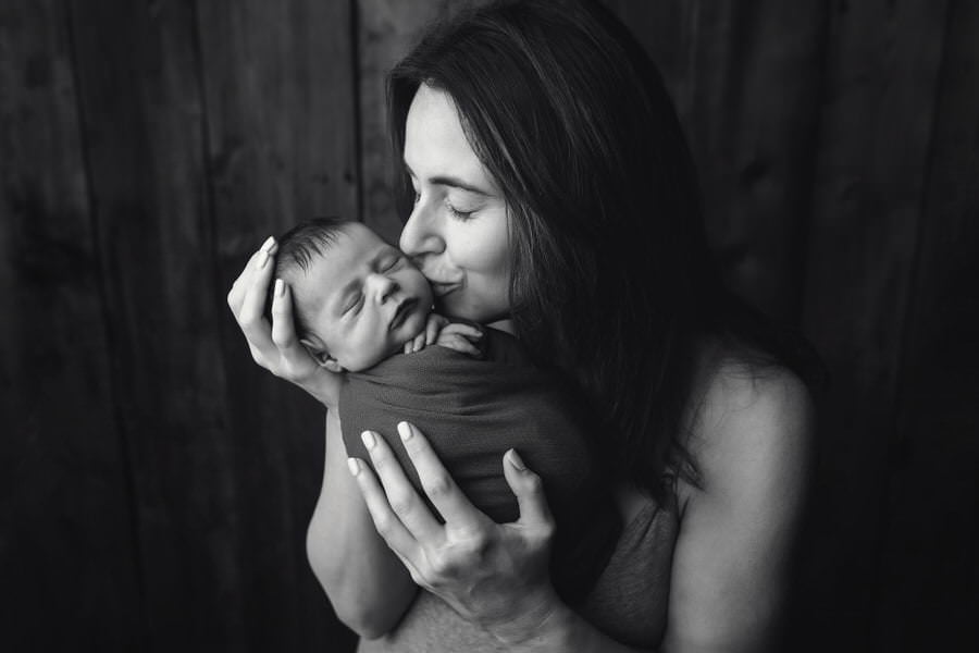 Black and white image of a Mother kissing her newborn baby boy during their photoshoot