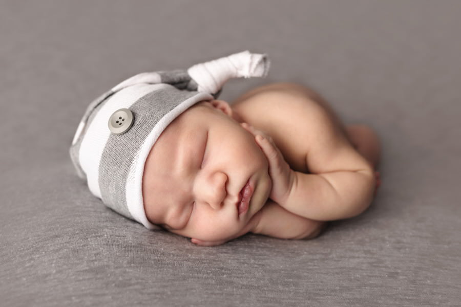 Sleeping newborn baby boy holds his cheeks lying on a gray blanket during his photoshoot