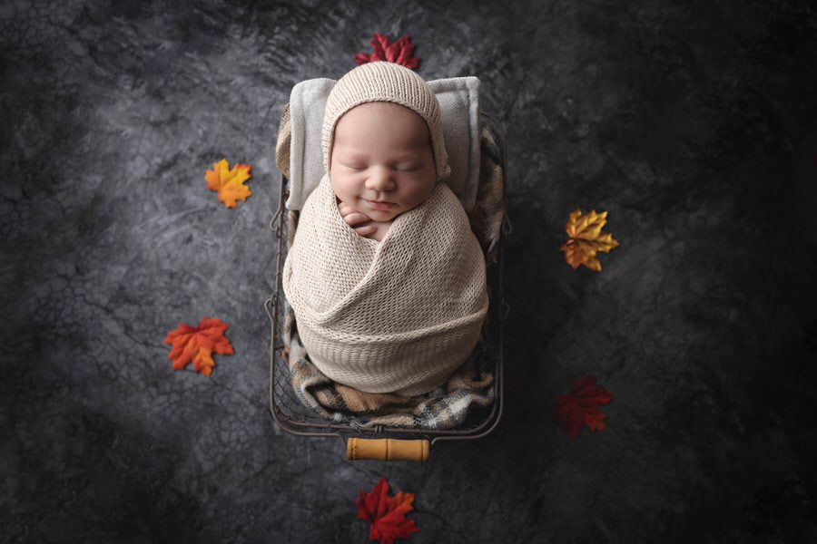 A sleeping newborn baby boy smiles lying in a basket during his photoshoot