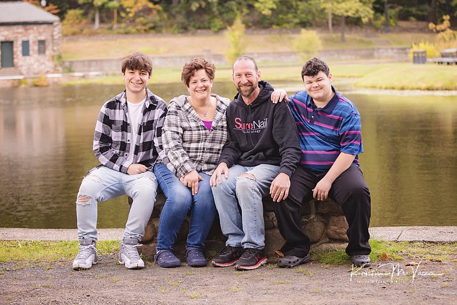 Family of 4 sitting on a bench in front of a pond during their twin boy senior photos