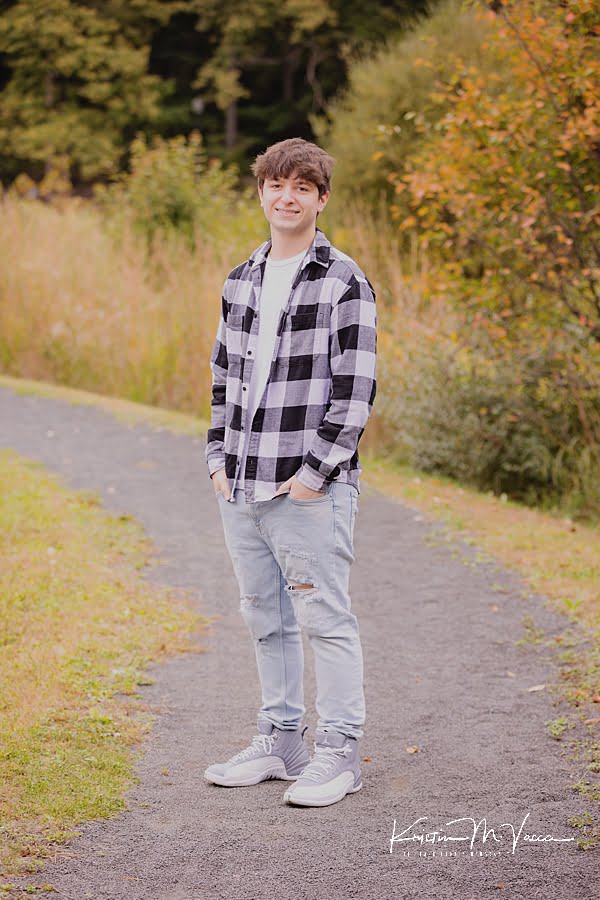 Teen boy poses standing on a path during his senior photoshoot