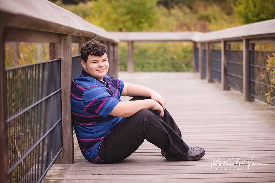 Teen boy sits against a boardwalk railing during his senior portraits
