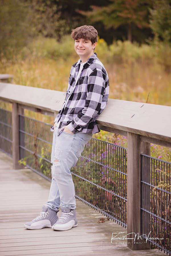 Teen boy leans standing against a railing during his portrait session