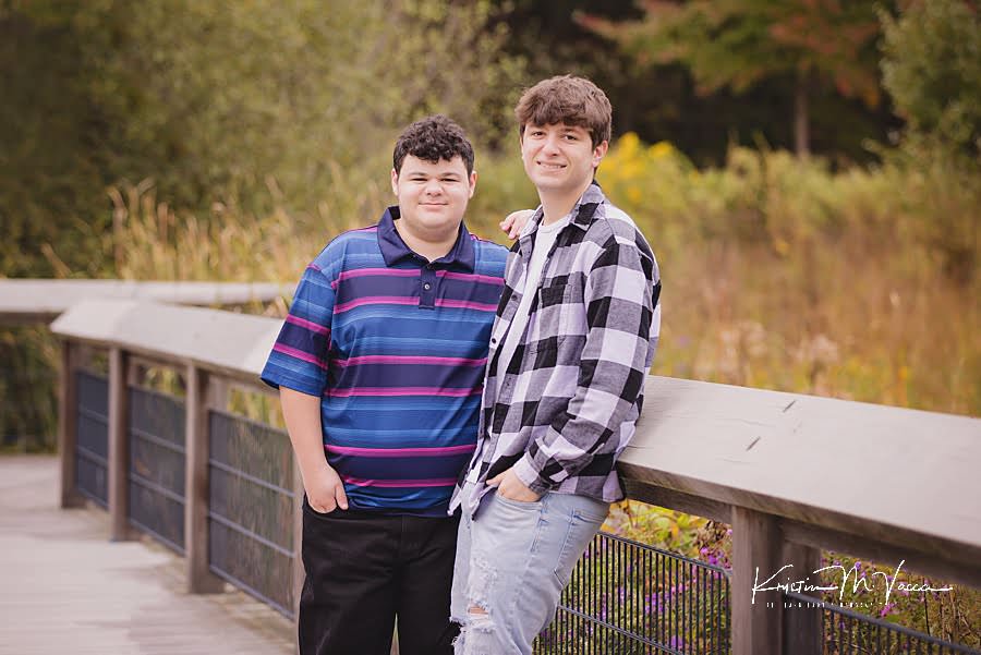 Teen brothers stand posing on a boardwalk during their twin boy senior photos