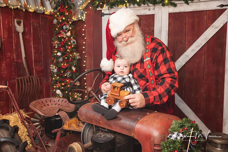 Santa Claus holds a baby sitting on a tractor at The Flash Lady Photography