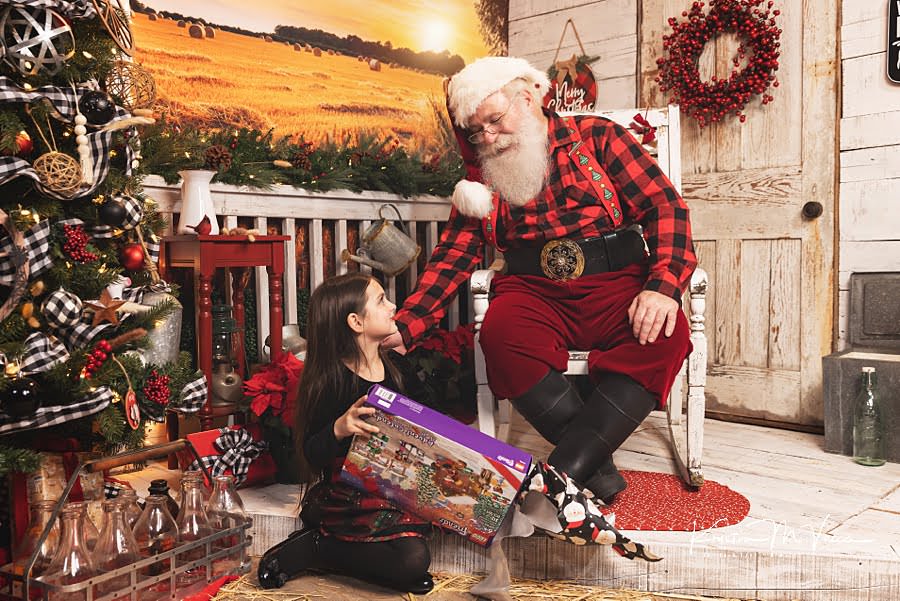 Santa Claus watches a young girl open her present during Christmas photos 2022