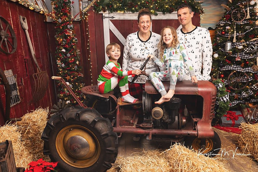 Twin brother and sister sit on a tractor with their parents during Christmas photos 2022 at The Flash Lady Photography