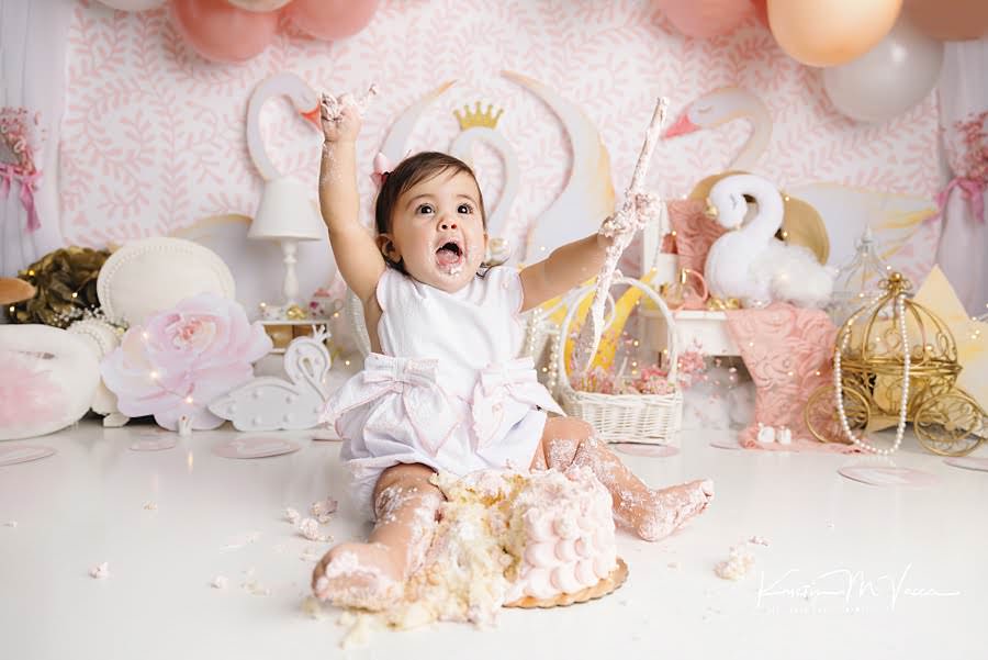 Toddler girl lifts her hands in joy during her grandmillennial swan princess cake smash